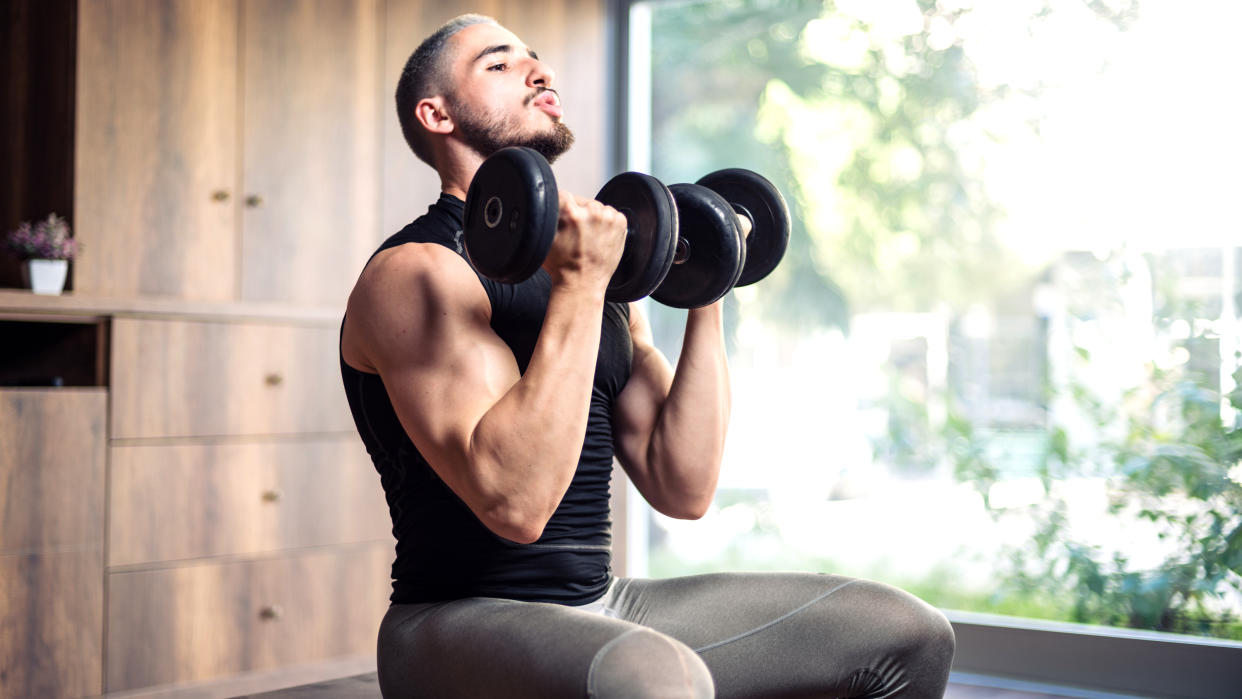  A man performing bicep curls on a bench with a pair of dumbbells. 