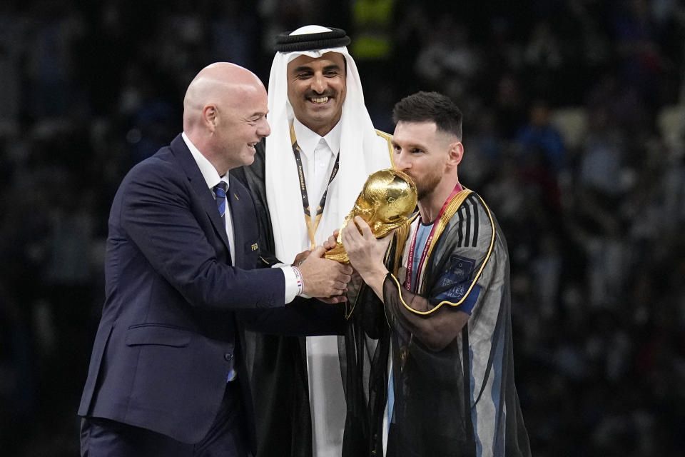 Argentina's Lionel Messi receives the trophy from FIFA President Gianni Infantino, left, and the Emir of Qatar Sheikh Tamim bin Hamad Al Thani, after winning the World Cup final soccer match between Argentina and France at the Lusail Stadium in Lusail, Qatar, Sunday, Dec. 18, 2022. Argentina won 4-2 in a penalty shootout after the match ended tied 3-3. (AP Photo/Martin Meissner)