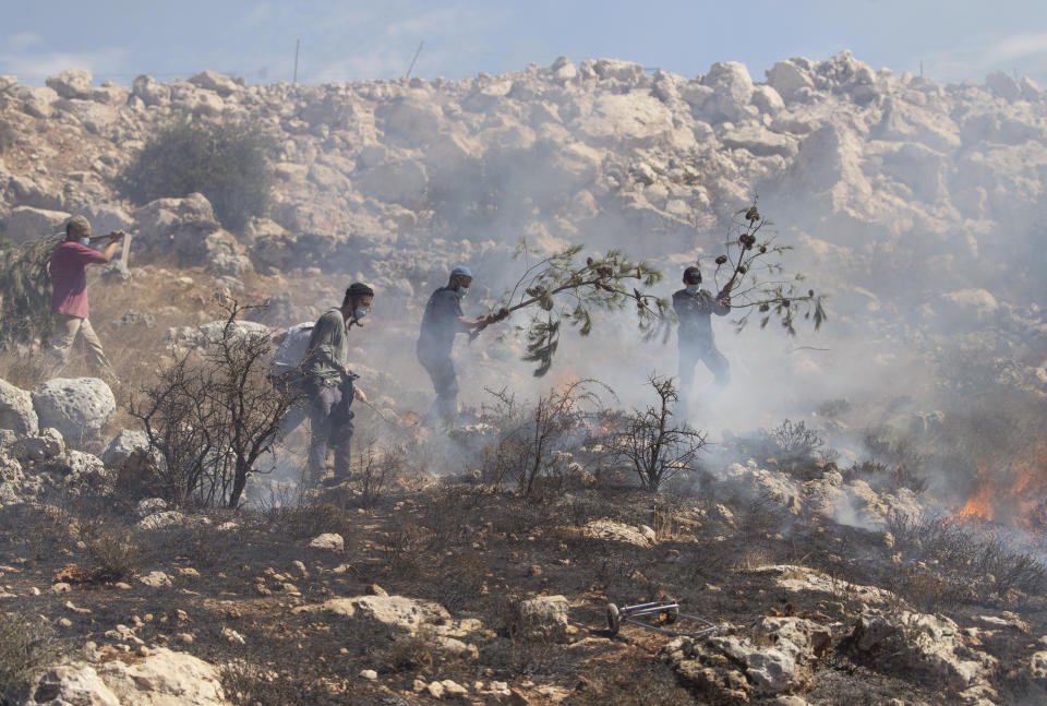 Jewish settlers fight fire in olive groves near their outpost that was caused by Israeli police's teargas canisters, used to disperse Palestinian farmers going to their groves, in the West Bank village of Burqa, East of Ramallah, Friday, Oct. 16, 2020. Palestinians clashed with Israeli border police in the West Bank on Friday during their attempt to reach and harvest their olive groves near a Jewish settlers outpost. (AP Photo/Nasser Nasser)