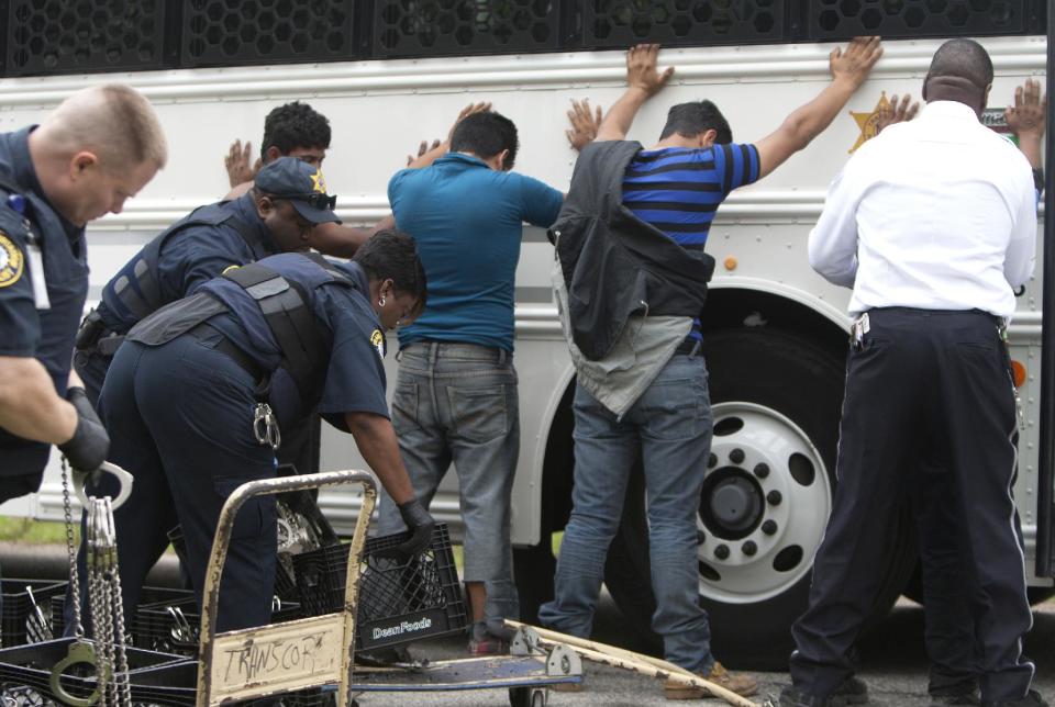 FILE - In this March 19, 2014 file photo, authorities search people outside a house in southeast Houston where more than 100 people in the United States illegally were discovered, according to police. Five men, at least two of them from Mexico, are accused of using guns and threats to hold 115 people hostage unless they paid ransom to continue their illegal entry into the United States. The five are scheduled to appear before a federal magistrate judge on Tuesday, March 25, 2014. (AP Photo/Houston Chronicle, Cody Duty, File)