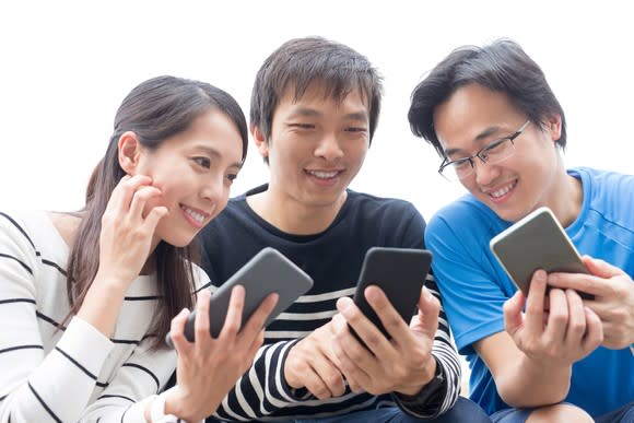 Three young people smiling and looking at each other's smartphones.