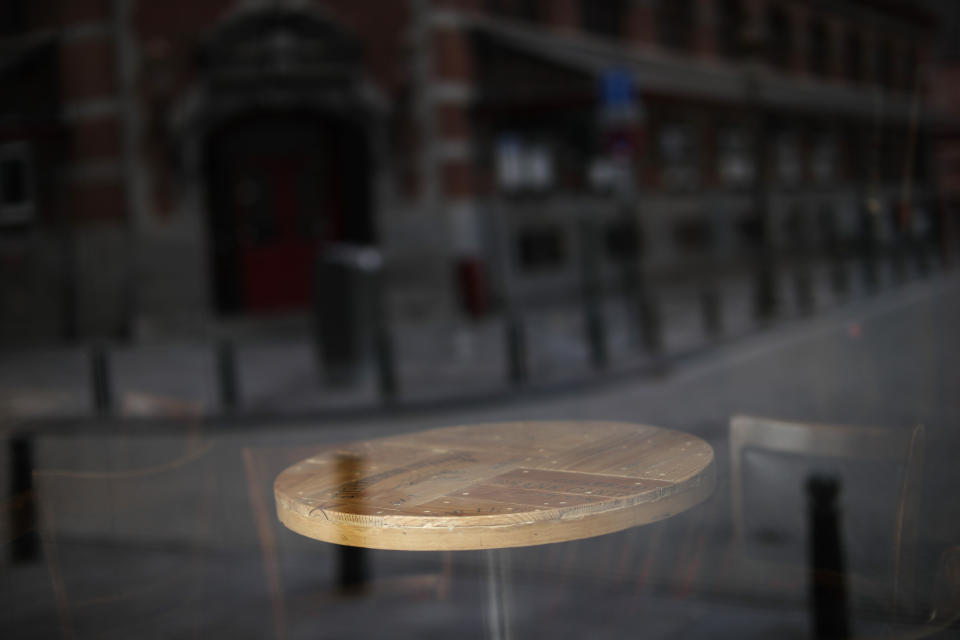 The empty table of a closed bar is seen through a window in downtown Brussels, Thursday, Oct. 8, 2020. Since bars in Brussels were forced to close as of Thursday for at least a month to deal with a massive surge in coronavirus cases while restaurants were allowed to remain open, the big question on the streets is: when is a bar a bar and when is a bar a restaurant. (AP Photo/Francisco Seco)