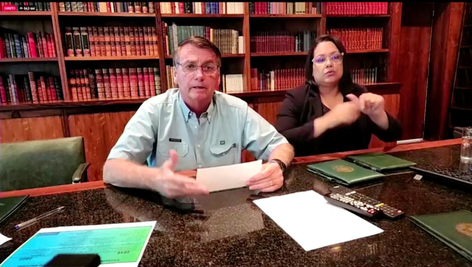 President Jair Bolsonaro speaks in a library setting at a conference table, with a woman sitting beside him.