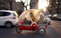 A woman and her son sit inside the capsule of an electric tricycle as they drive along a main road in central Beijing March 15, 2012.