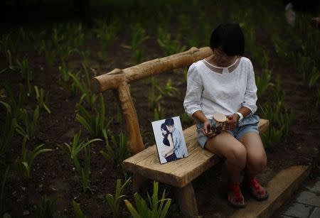 Cheng Liping, whose husband Ju was onboard Malaysia Airlines Flight MH370 which disappeared on March 8, 2014 shows a picture which features she and her husband together, and her husband's cup, at a park near her house where she and her husband used to visit during an interview with Reuters in Beijing July 24, 2014. REUTERS/Kim Kyung-Hoon/Files