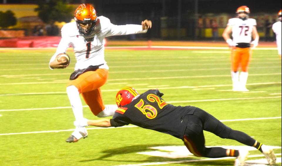 Merced High School quarterback Quintell Dupree (1) leaps to avoid Oakdale senior Gage Ginger (52) during a playoff game on Friday, Nov. 11, 2023.