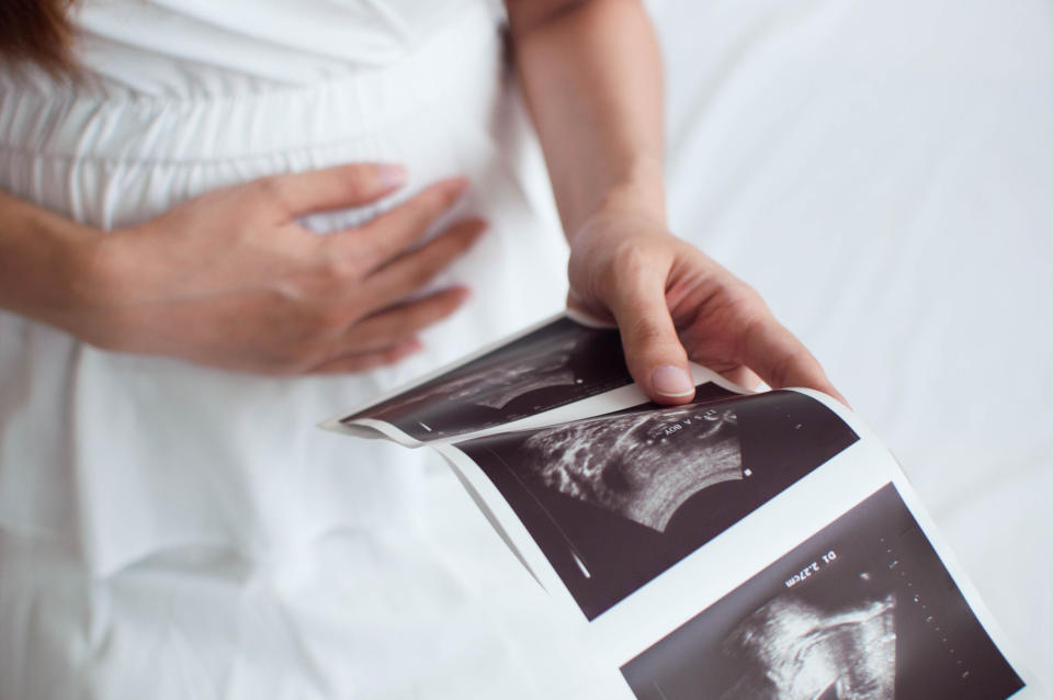 Someone holds their pregnant  stomach while looking at an ultrasound