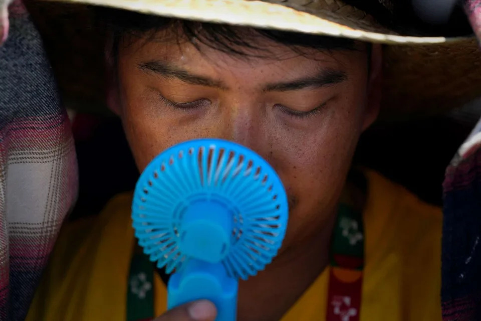 PHOTO: A World Youth Day volunteer uses a small fan to cool off from the intense heat, just outside Lisbon, Portugal, Aug. 6, 2023. (Armando Franca/AP)