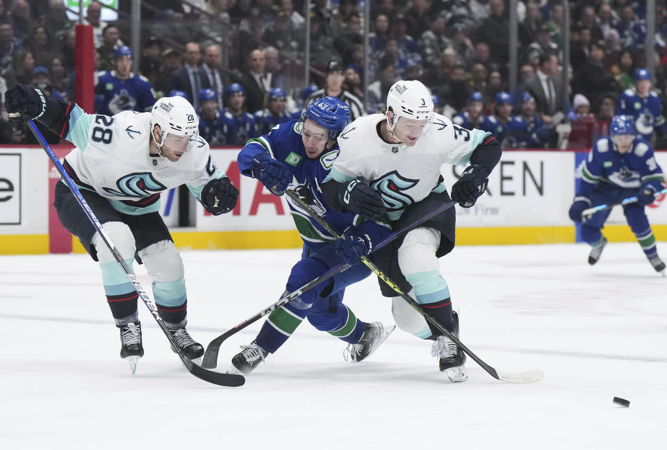 Vancouver Canucks' Quinn Hughes, center, is checked by Seattle Kraken's Will Borgen, right, in front of Carson Soucy during the third period of an NHL hockey game Tuesday, April 4, 2023, in Vancouver, British Columbia. (Darryl Dyck/The Canadian Press via AP)