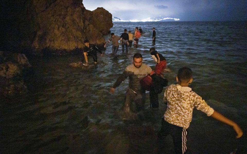 Migrants walk into shallow waters on the shore of the northern town of Fnideq  - AFP/ Fadel Senna