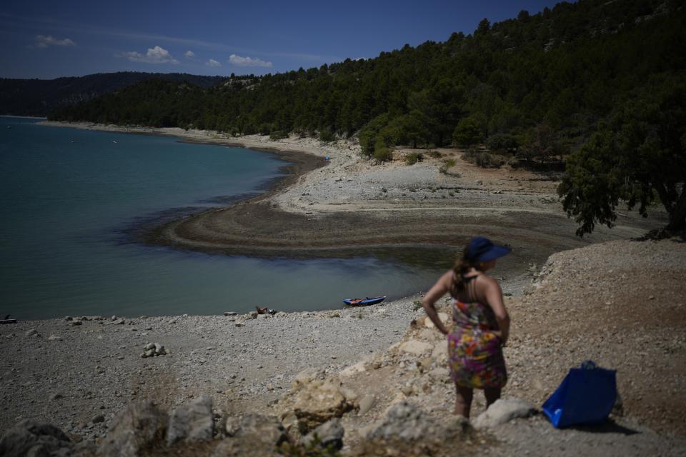 FILE - A sunbather stands in front of the receding water line of the Verdon Gorge, southern France, Tuesday, Aug. 9, 2022. Earth’s fever persisted last year, not quite spiking to a record high but still in the top five or six warmest on record, government agencies reported Thursday, Jan. 12, 2023. (AP Photo/Daniel Cole, File)