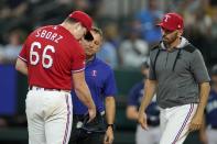 Texas Rangers starting pitcher Josh Sborz (66) is checked on by athletic trainer Matt Lucero, center, and manager Chris Woodward after Sborz was struck by the ball on a single by Seattle Mariners' Mitch Haniger during the first inning of a baseball game in Arlington, Texas, Friday, Aug. 12, 2022. (AP Photo/Tony Gutierrez)