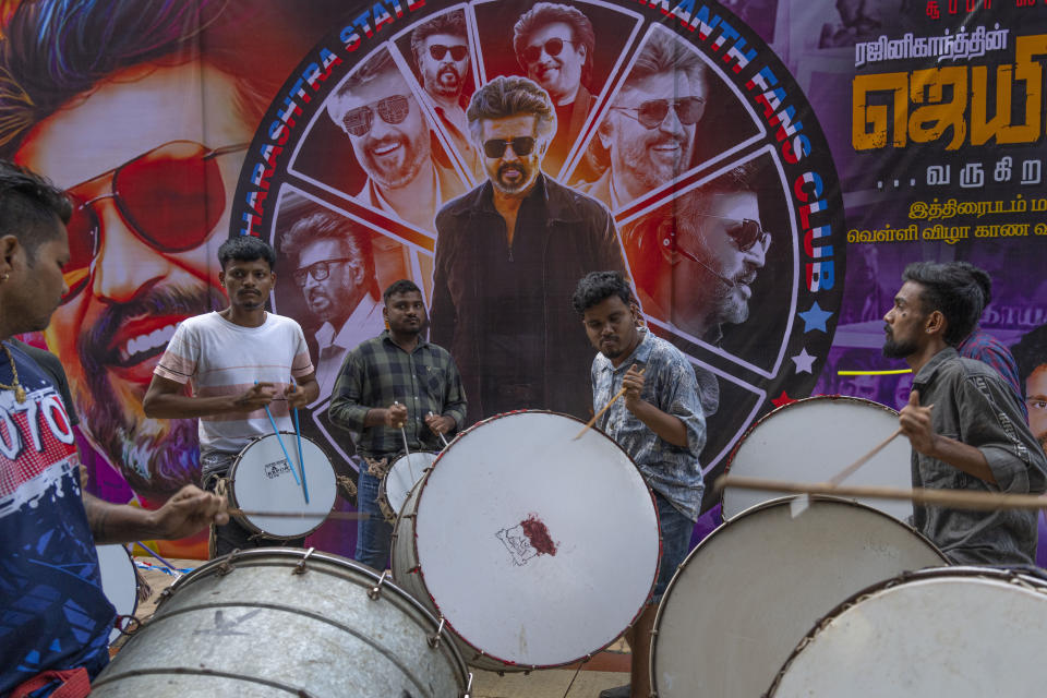 Drummers play near a poster of Indian superstar Rajinikanth, outside a cinema hall as fans celebrate the screening of his latest film "Jailer" in Mumbai, India, Thursday, Aug. 10, 2023. (AP Photo/Rafiq Maqbool)