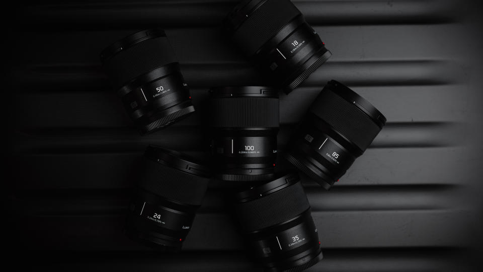 Panasonic Lumix S 100mm f2.8 Macro lens surrounded by other Panasonic lenses in a dark environment