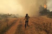 A man runs as fire burns trees in Kirinthos village on the island of Evia, about 135 kilometers (84 miles) north of Athens, Greece, Friday, Aug. 6, 2021. Thousands of people fled wildfires burning out of control in Greece and Turkey on Friday, including a major blaze just north of the Greek capital of Athens that claimed one life, as a protracted heat wave left forests tinder-dry and flames threatened populated areas and electricity installations. (AP Photo/Thodoris Nikolaou)