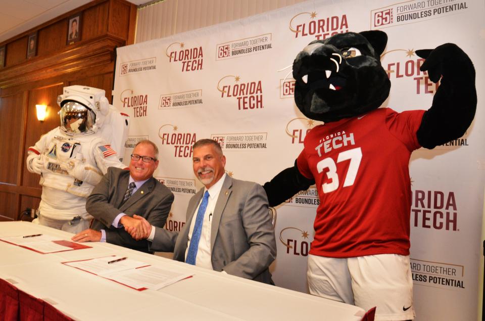 Flanked by mascots SpacePerson and Pete the Panther, Kennedy Space Center Visitor Complex Chief Operating Officer Therrin Protze and Florida Tech President John Nicklow sign the astronomy agreement Monday.