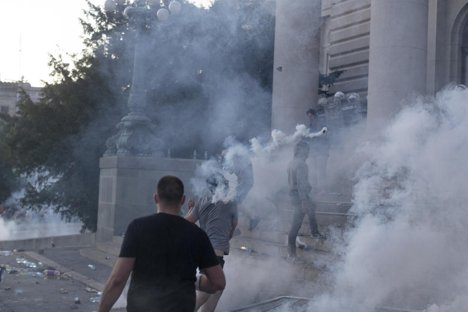 A man hurls a tear gas canister at riot police on the steps of the Serbian parliament during a protest in Belgrade, Serbia, Wednesday, July 8, 2020. Police have fired tear gas at protesters in Serbia's capital during the second day of demonstrations against the president's handling of the country's coronavirus outbreak. President Aleksandar Vucic backtracked on his plans to reinstate a coronavirus lockdown in Belgrade this week, but it didn't stop people from firing flares and throwing stones while trying to storm the downtown parliament building. (AP Photo/Marko Drobnjakovic)