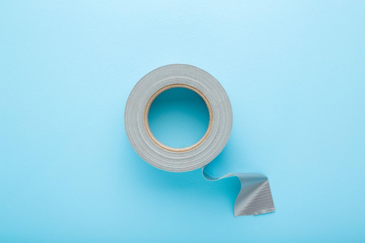 One roll of silver cloth duct tape on light blue table background. Pastel color. Closeup. Top down view.