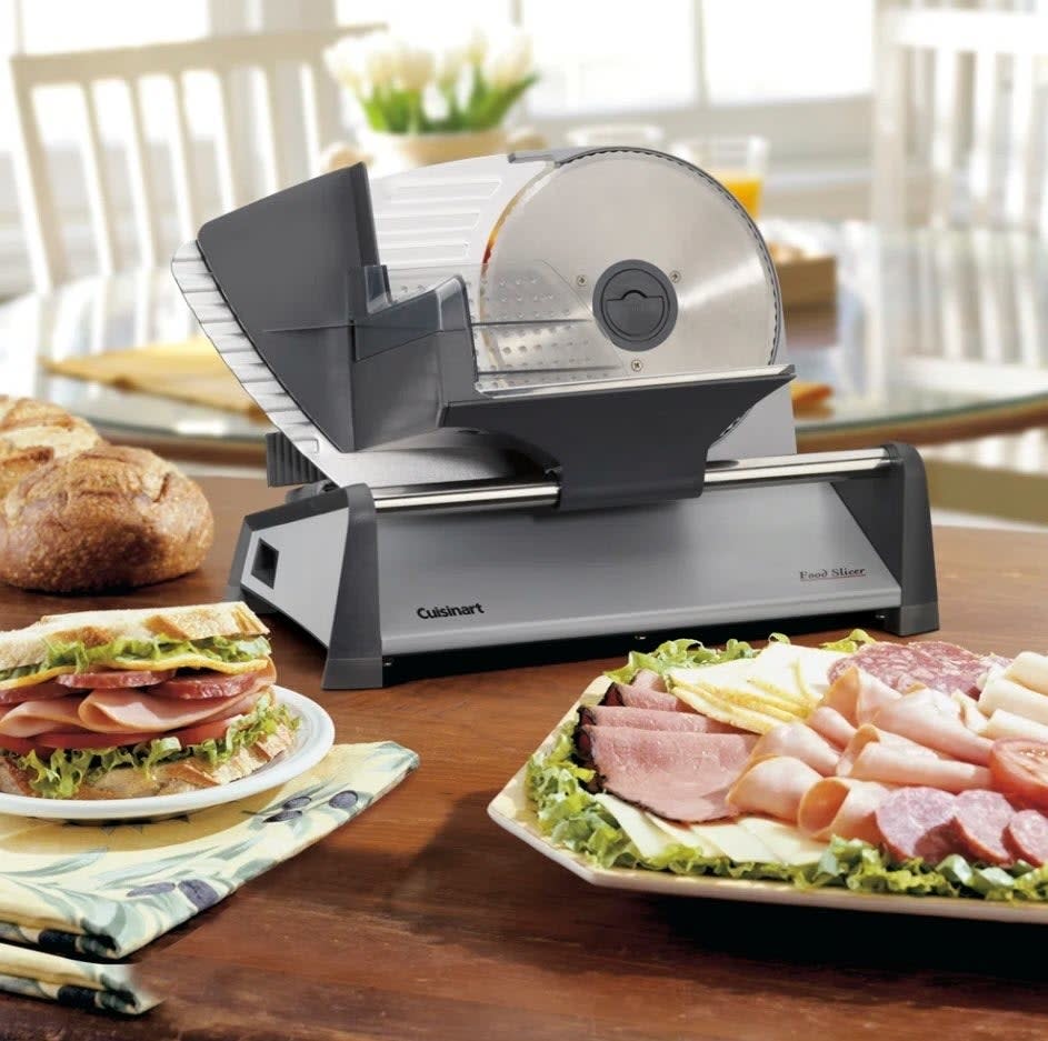 Cuisinart food slicer on a table with sliced bread, meats, and salad in the foreground