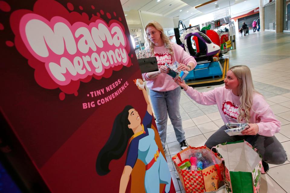 Kelly Walton and her sister Kristy Walton load their Mama Mergency vending machine with items that a mother with young child might need, at the Dartmouth Mall. In the background a woman pushes a baby carriage into the mall's main corridor.