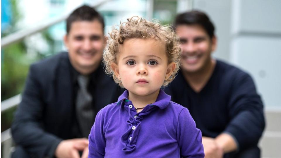 Un niño delante de sus padres.