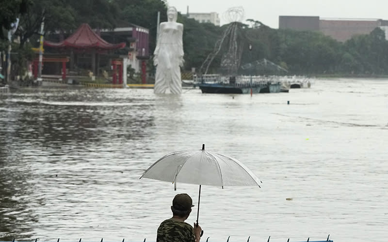 A man with an umbrella stands in the foreground looking toward a flooded park in the background