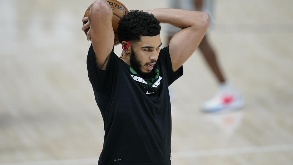 Jayson Tatum stretches his arms behind his head with a ball in his hand during warmups.