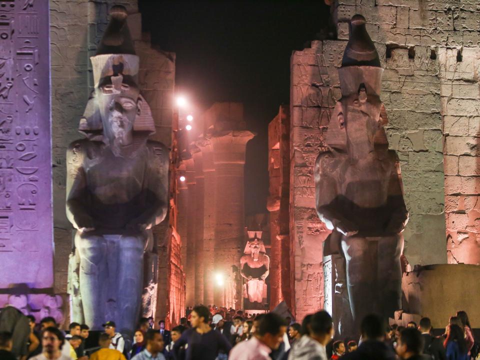 Visitors walk past the statues of the Ancient Egyptian New Kingdom Pharaoh Ramses II (1303-1213 BC) at night at the Temple of Luxoron November 25, 2021 in Luxor, Egypt.