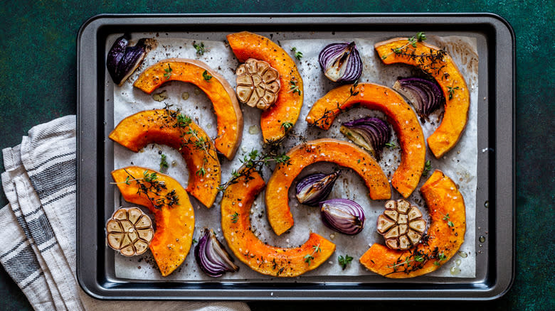 Butternut squash, garlic heads, and red onion on a baking pan