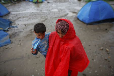 A refugee woman carrying her child walks under heavy rainfall at a makeshift camp for migrants and refugees at the Greek-Macedonian border near the village of Idomeni, Greece, May 21, 2016. REUTERS/Kostas Tsironis