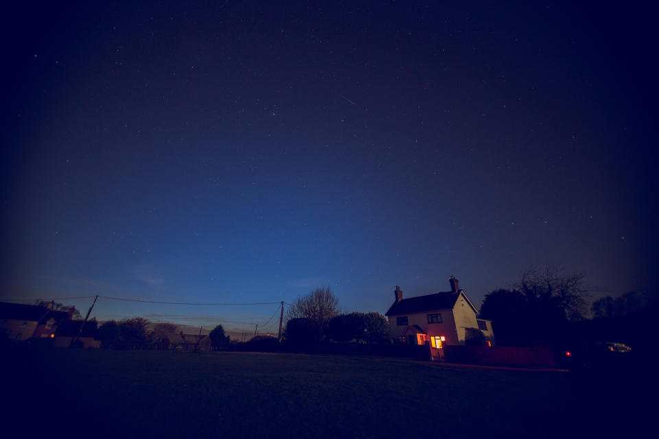 A house with its lights on is seen from a distance in a dark neighborhood