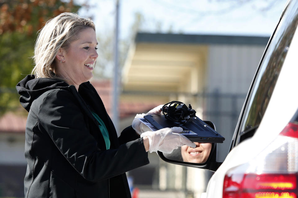 Lindsey Lilley, an employee of the Elk Grove Unified School District, hands a Chromebook to the parent of a student in the district, at Monterey Trail High School in Elk Grove, Calif., Thursday, April 2, 2020. In response to the order to close school buildings to the public, due to the coronavirus, the laptops are being loaned to qualifying district families as part of the district's "distance learning" program which will be ready to go live by mid-April. (AP Photo/Rich Pedroncelli)