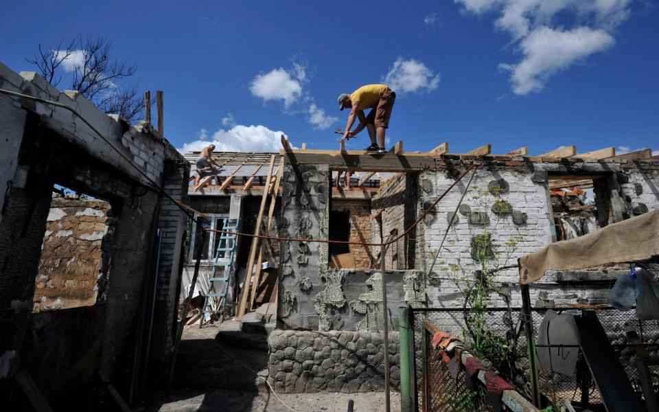 A volunteer repairs the roof of the house of an elderly woman, after it was destroyed by shelling in the village of Zalissya, Kyiv - SERGEI CHUZAVKOV/AFP