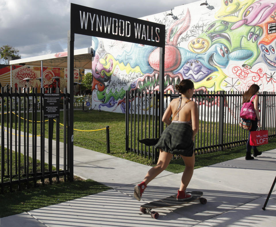 A skateboarder and pedestrian pass the entrance to Wynwood Walls, Monday, Dec. 3, 2012 in Miami. Art Basel Miami Beach and about two dozen other independent art fairs open Thursday. Tens of thousands of people are expected through Sunday at the fairs throughout Miami and South Beach. Street artists, including Shepard Fairey, have painted colorful new works onto the exteriors of the warehouses and building of the Wynwood district. (AP Photo/Wilfredo Lee)