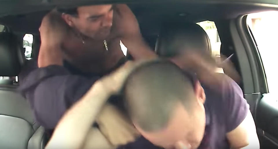 The passenger leans over from the backseat and attacks the driver.