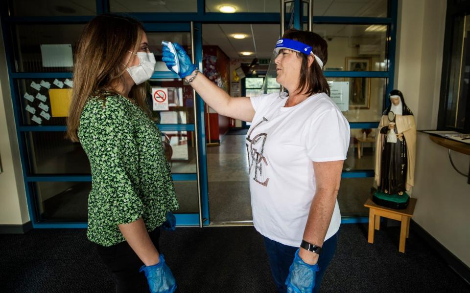 Teacher Catherine McClean has her temperature checked by assistant teacher Hilary Brennan at St Clare's Primary School in Belfast - Liam McBurney/PA Wire