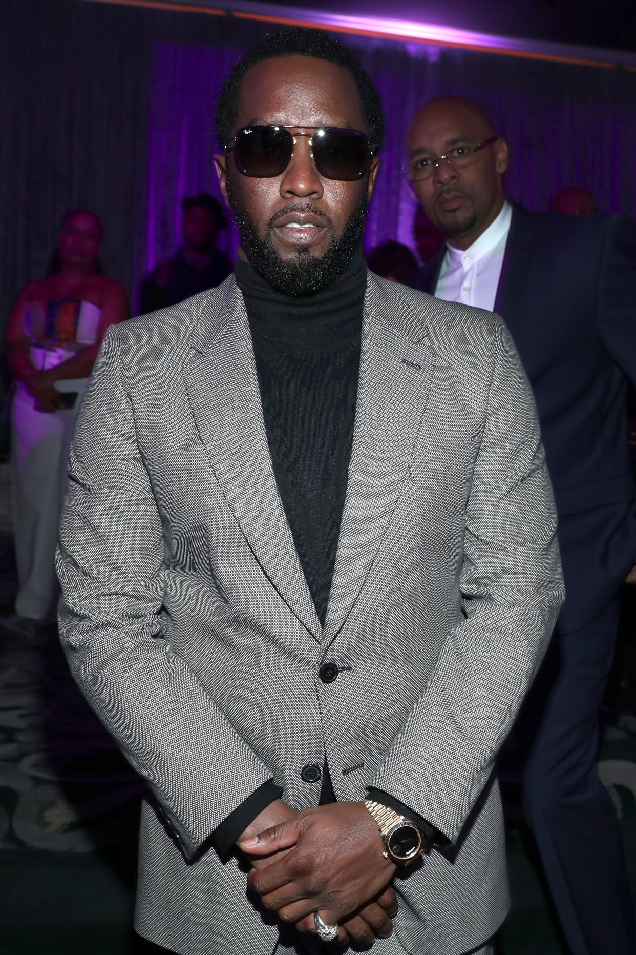 Diddy looks elegant in this grey suit and pant with his hands crossed in front of him. 