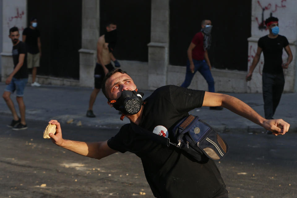 Anti-government protesters throw stones toward riot police during a protest marking the first anniversary of the massive blast at Beirut's port, near Parliament Square, In Beirut, Lebanon, Wednesday, Aug. 4, 2021. United in grief and anger, families of the victims and other Lebanese came out into the streets of Beirut on Wednesday to demand accountability as banks, businesses and government offices shuttered to mark one year since the horrific explosion. (AP Photo/Bilal Hussein)