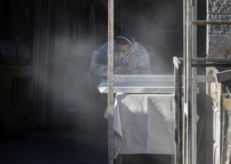 Sun Valley, CA - October 31: Stone countertop fabricator creates a cloud of dust while wearing a mask to help protect against airborne particles which can contribute to silicosis at a shop on Tuesday, Oct. 31, 2023 in Sun Valley, CA. (Brian van der Brug / Los Angeles Times)