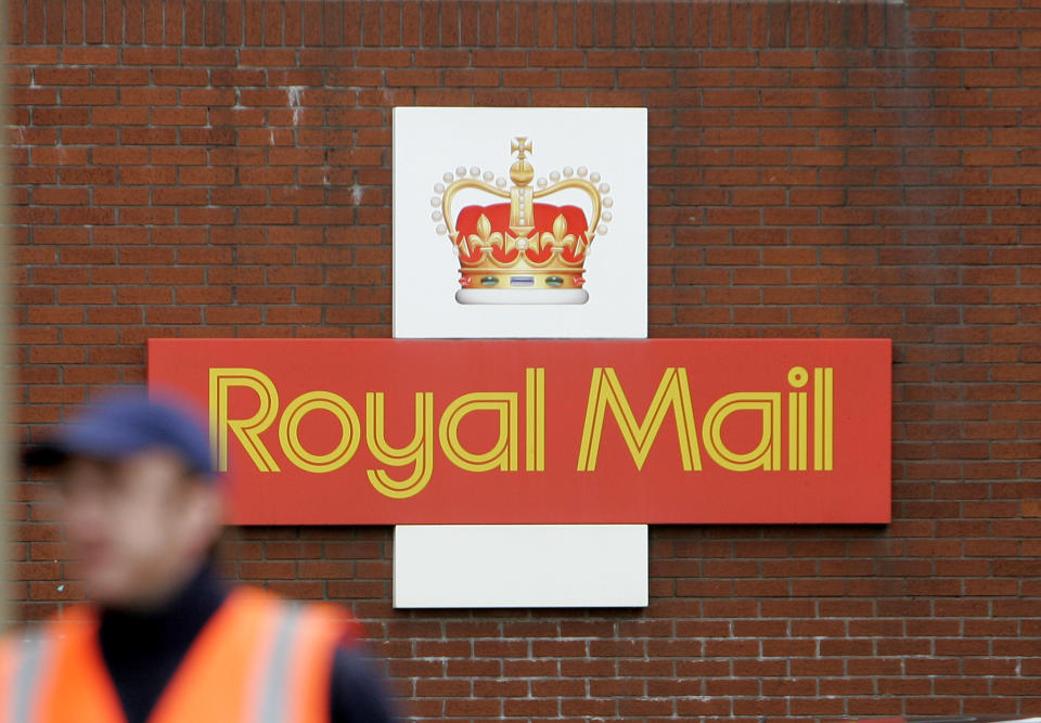 A British Royal Mail logo is seen behind a postal worker walking at a delivery office in London, Monday, Oct. 19, 2009. Royal Mail and the Communication Workers Union (CWU) have resumed talks on pay and working reforms on Monday aimed at avoiding national strikes planned on Thursday and Friday of this week,  while Royal Mail management is planning to hire up to 30,000 temporary workers. (AP Photo/Akira Suemori)