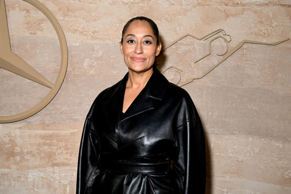 Tracee in satin jacket posing against an emblem-decorated backdrop