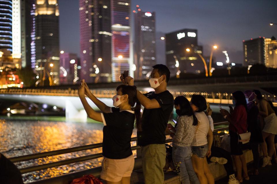 SINGAPORE - 2020/08/09: A couple wearing face masks as a preventive measure take pictures at the esplanade, located along the Singapore River during the Singapore National Day. Singapore celebrates its 55th National Day on the 9th of August 2020 amid the Covid-19 pandemic. (Photo by Maverick Asio/SOPA Images/LightRocket via Getty Images)