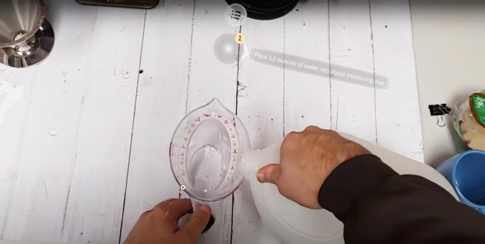 First-person view of a person pouring liquid from a plastic jug into a measuring cup. AR instructions to “Pour 12 ounces of water into liquid measuring cup” are overlaid onto their field of view.