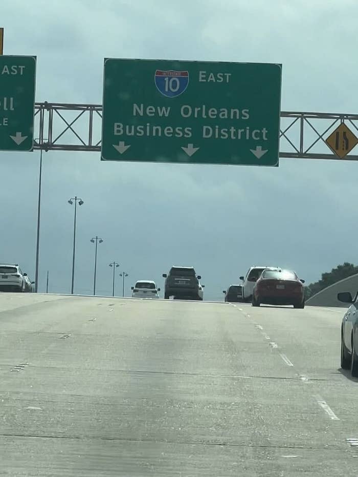 Highway view showing Interstate 10 East sign directing to New Orleans Business District. Multiple cars driving in both lanes