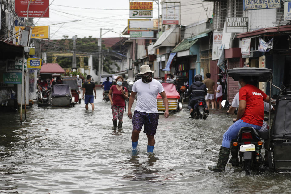 Residents wearing masks to prevent the spread of the coronavirus wade through a flooded road from Typhoon Molave in Pampanga province, northern Philippines on Monday, Oct. 26, 2020. The fast moving typhoon has forced thousands of villagers to flee to safety in provinces. (AP Photo/Aaron Favila)