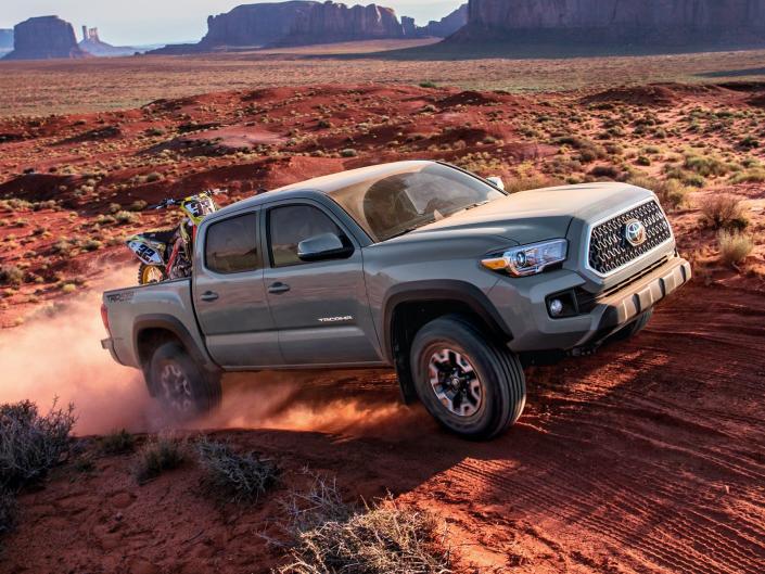 A gray Toyota Tacoma truck driving up red sand and rocks.