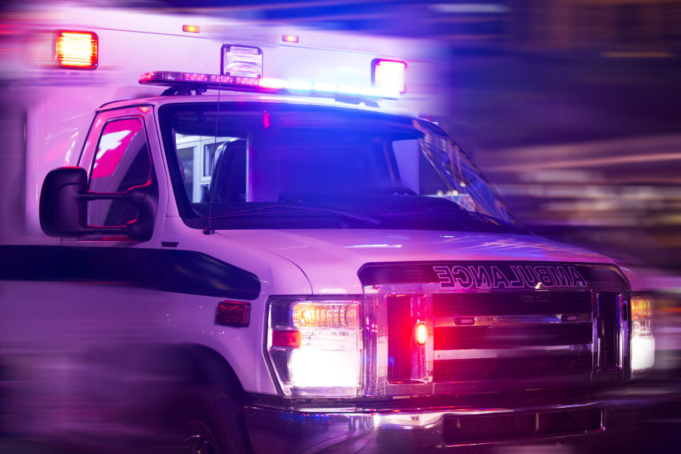 An ambulance with flashing lights is seen driving through a city at night