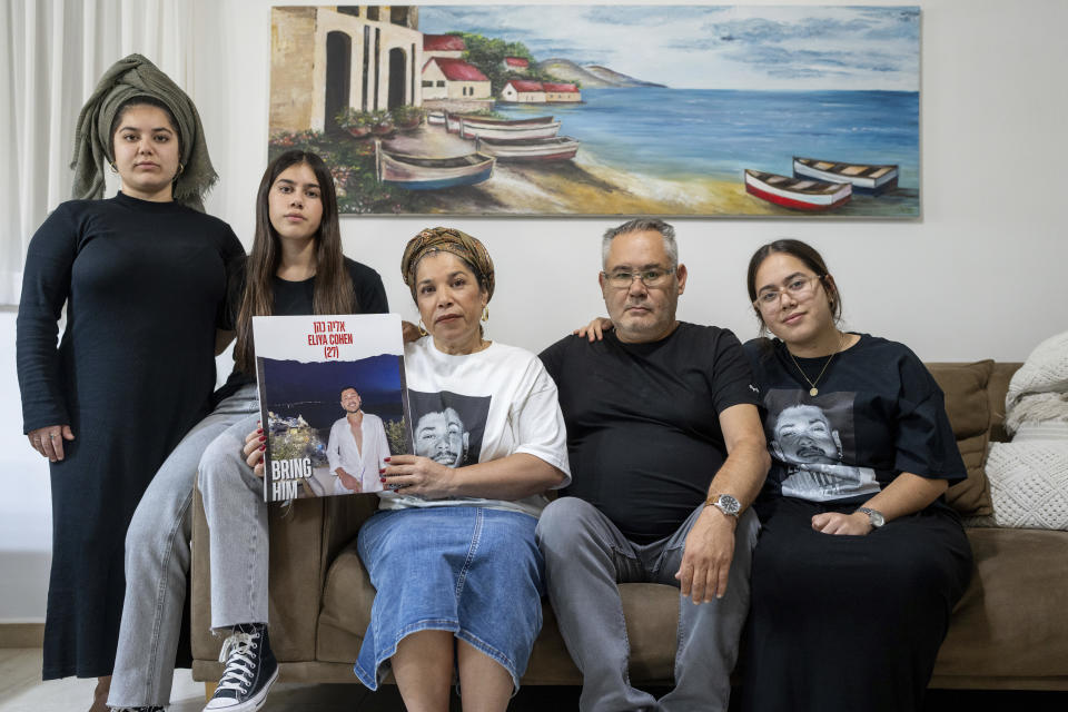 CORRECTS CONTEXT - Sigi and Momi Cohen, flanked on the couch by their children Yuval, Michal, and Tamar, hold up a portrait of their 27-year-old son, Eliya Cohen, in the family house in the village of Tzur Hadassah, Israel, Monday, Oct. 30, 2023. Cohen, an Israeli citizen, was abducted by Hamas militants from the "Nova" Music Festival near Kibbutz Re'im, Hamas fighters during the group's attack on Oct. 7 that resulted in the killing of over 1,400 people and the abduction of over 220. (AP Photo/Ohad Zwigenberg)