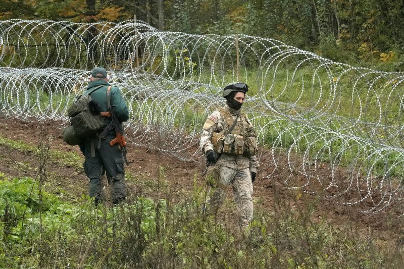 FILE PHOTO: A Latvian border guard and an army serviceman walk past temporary barbed wire fencing along the Latvian-Belarus border near Robeznieki, Latvia
