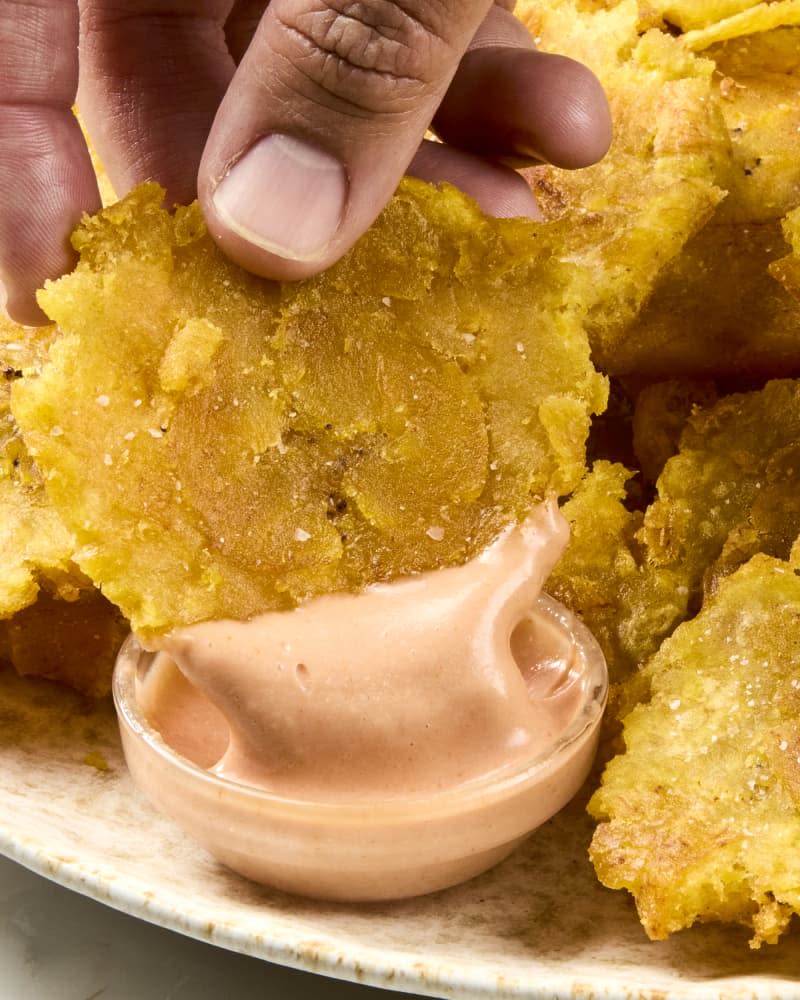 Closeup of a hand dipping a toston into a small bowl of dipping sauce.